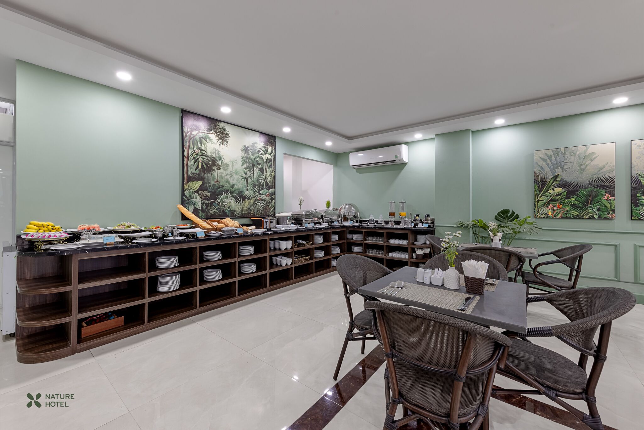 A hotel dining area with a buffet setup, wicker chairs, and green walls.