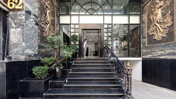 Una imponente entrada con escalones de mármol, una escalera y un amplio ventanal de cristal en arco.