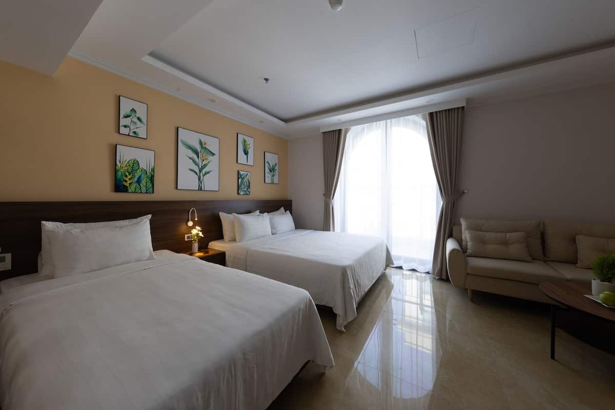 A hotel room with two beds, a sofa, and a nightstand with a lamp.