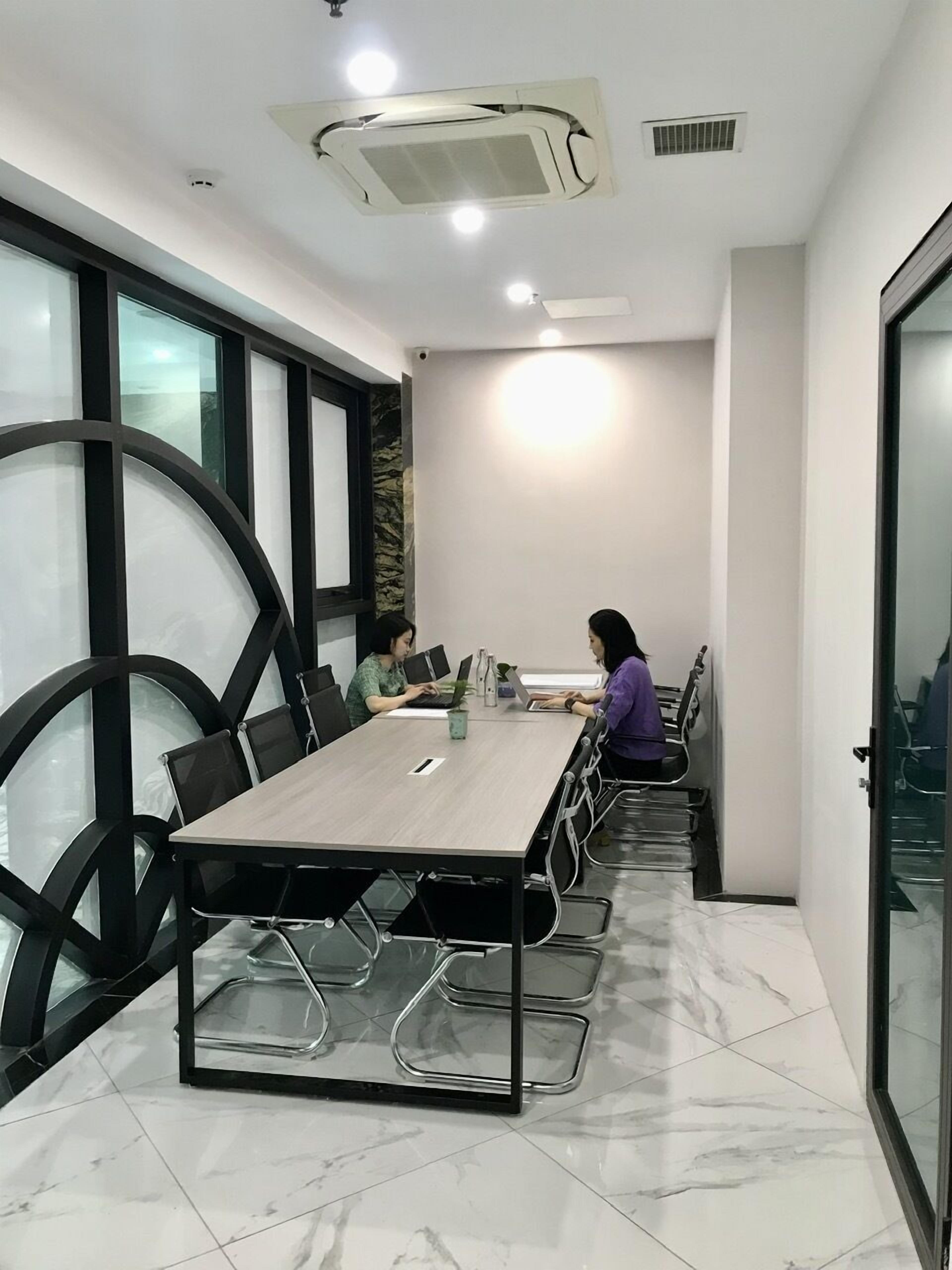 A conference room with a long table, chairs, and a person working on a laptop.