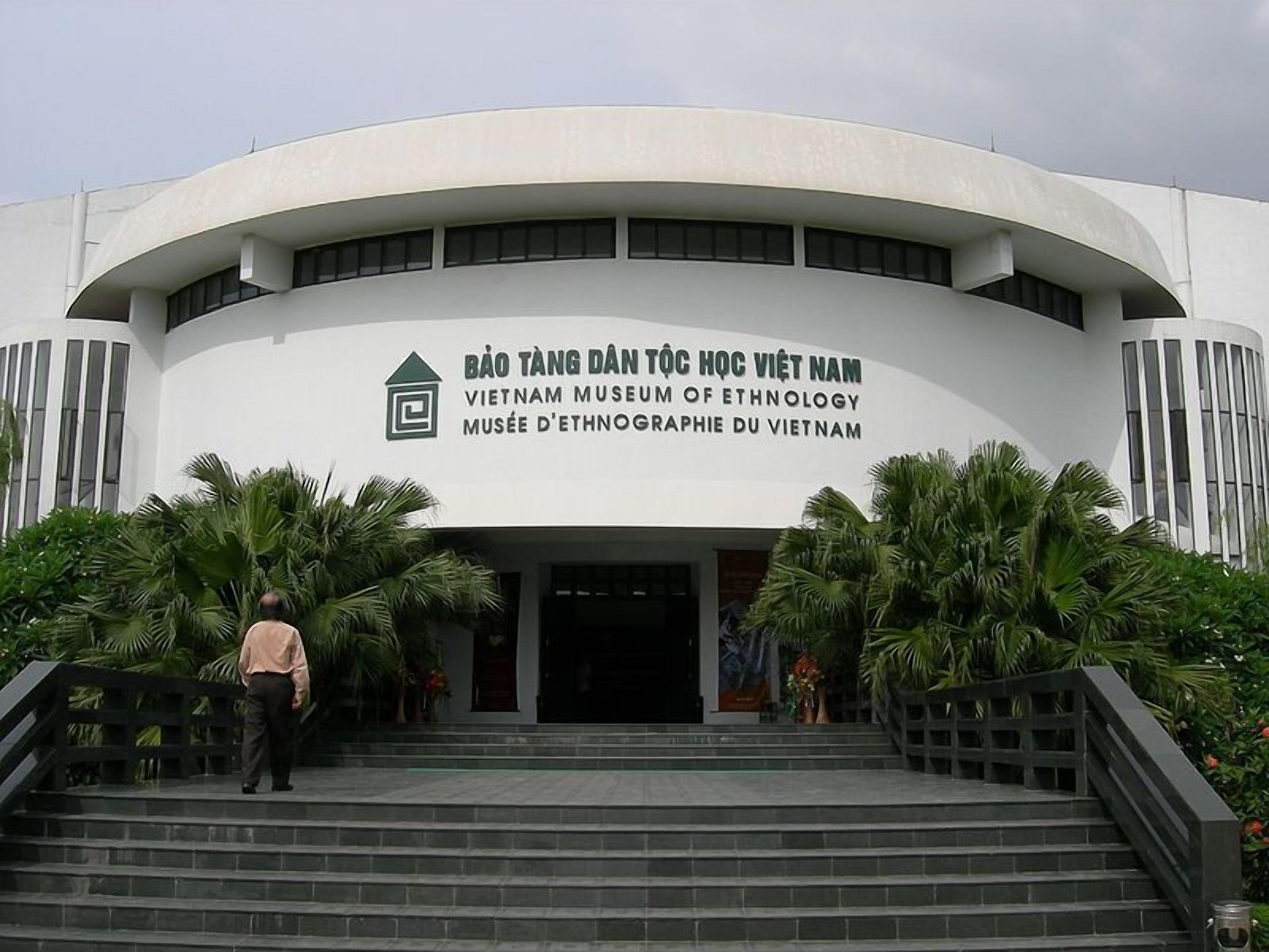 La entrada al Museo Etnológico de Vietnam, con una fachada curva, escalones que conducen a la entrada y palmeras en primer plano.