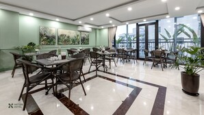 Un comedor de hotel con mesas y sillas, un ventanal con vistas, y una pared verde con obras de arte.