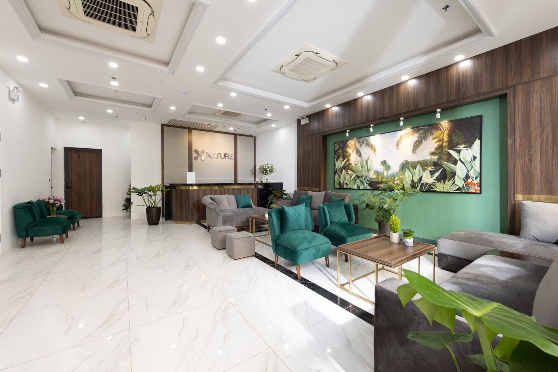 Un vestíbulo amplio con mostrador de recepción, sofás tapizados en verde y una gran pintura botánica en la pared.