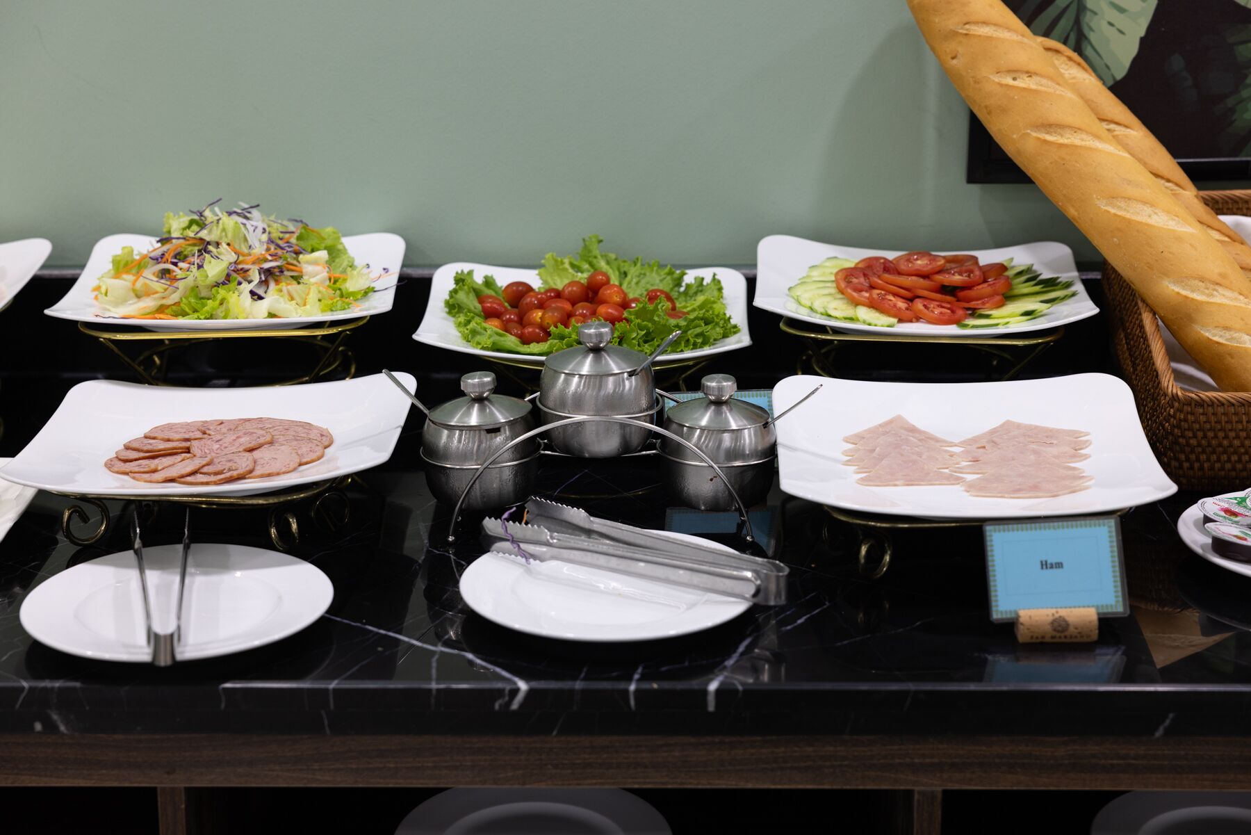 Una mesa de buffet con diversos alimentos, entre ellos ensaladas, carnes en rodajas y pan.