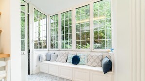 A room with a white bench along a window with multiple panes, a patterned floor, and a white door.