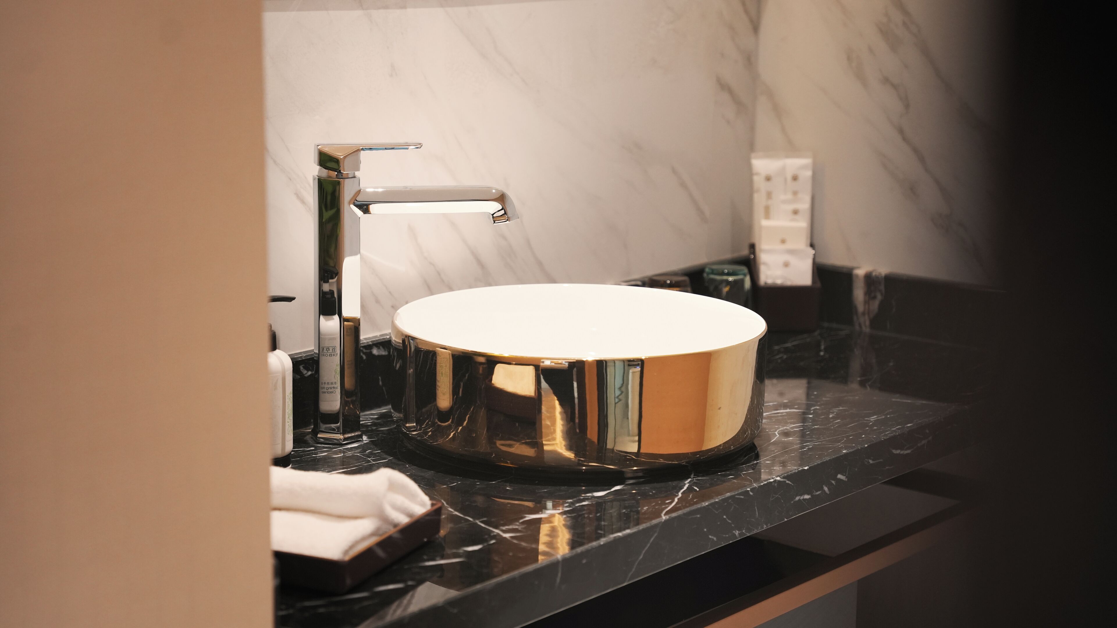A modern bathroom with a round, reflective sink, chrome faucet, and marble countertop.