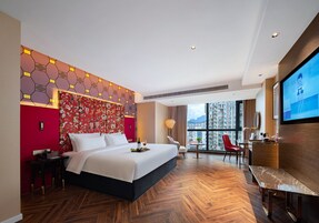 Una habitación de hotel moderna con una cama grande, un televisor, un escritorio y vistas a la ciudad.
