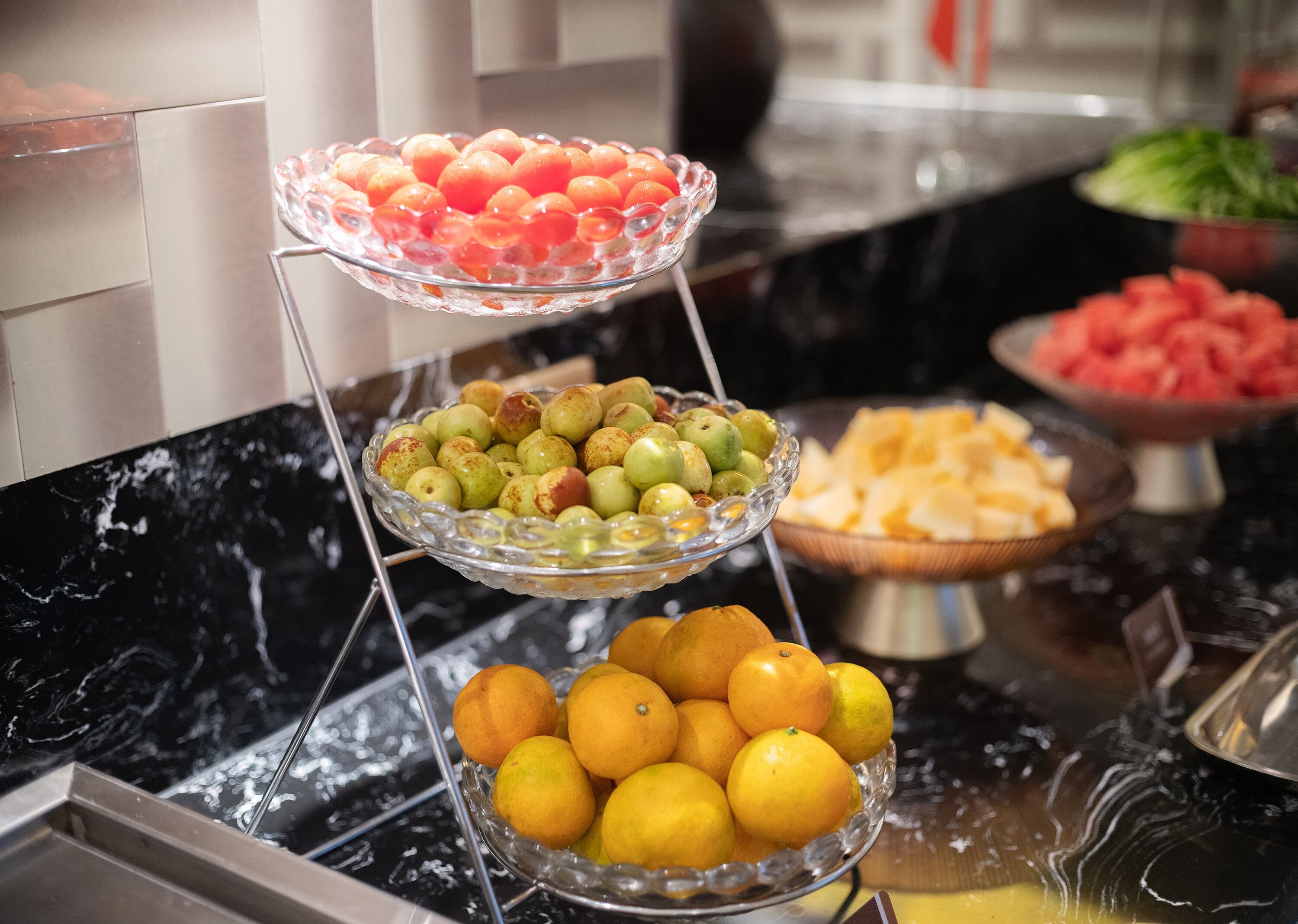 Un bufé con múltiples fuentes de vidrio que contienen diversas frutas y verduras.