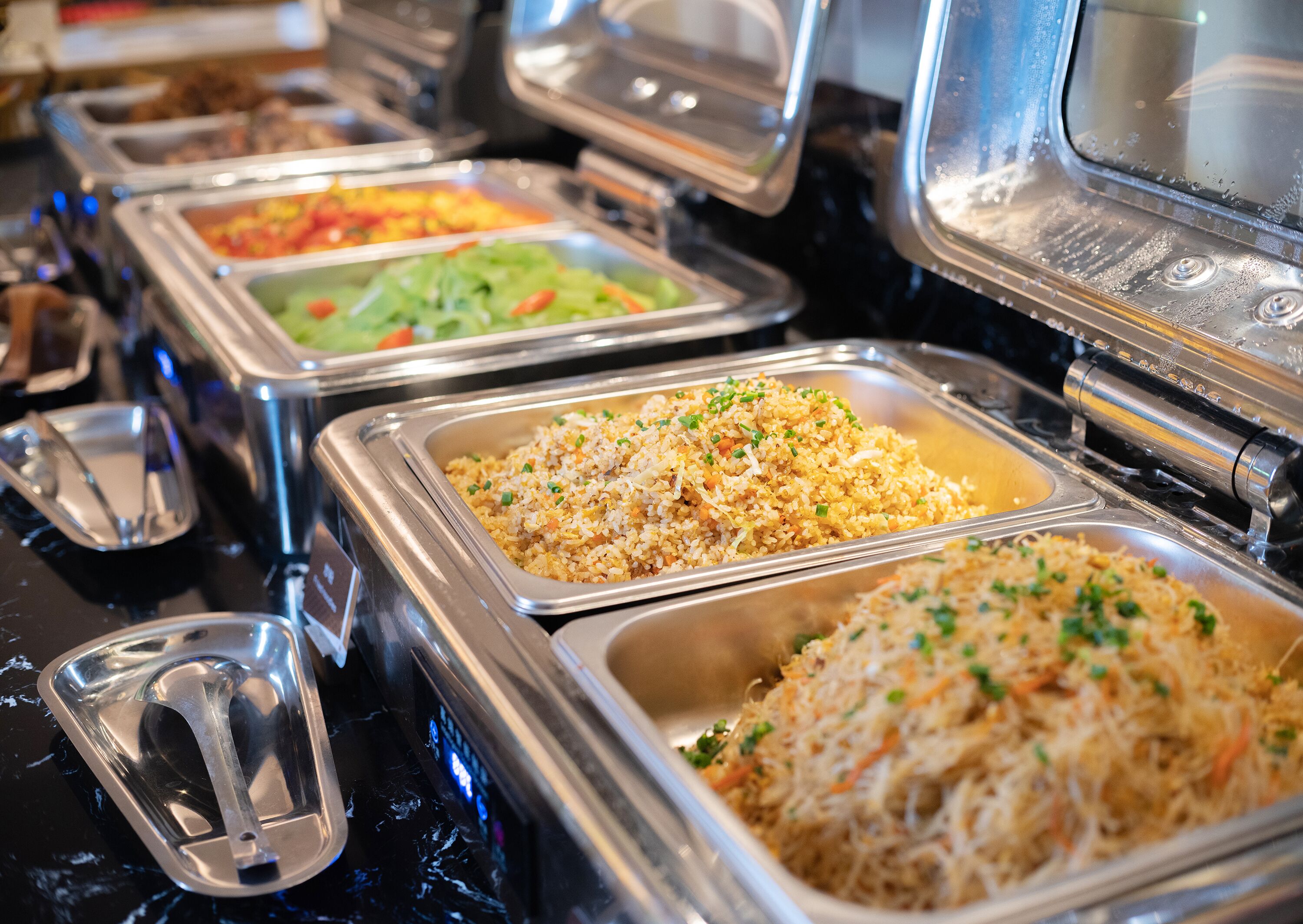 A buffet with various food options, including fried rice and salads.