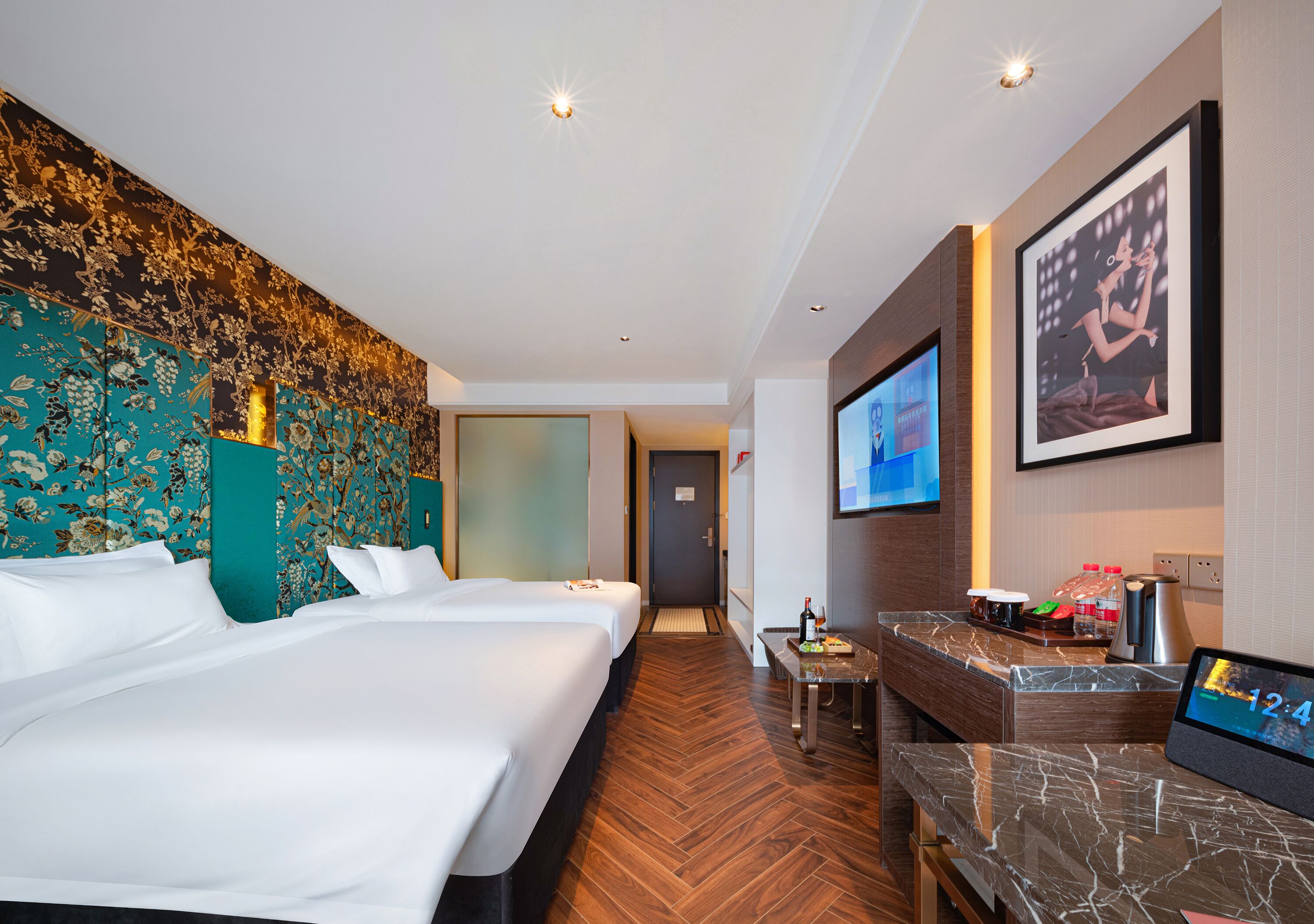 Ein Hotelzimmer mit zwei Betten, einem Schreibtisch mit Kaffeemaschine, einem Fernseher und einer digitalen Uhr.