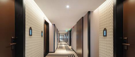 A hotel corridor with patterned walls, doors with keypads, and a carpet with a striped design.