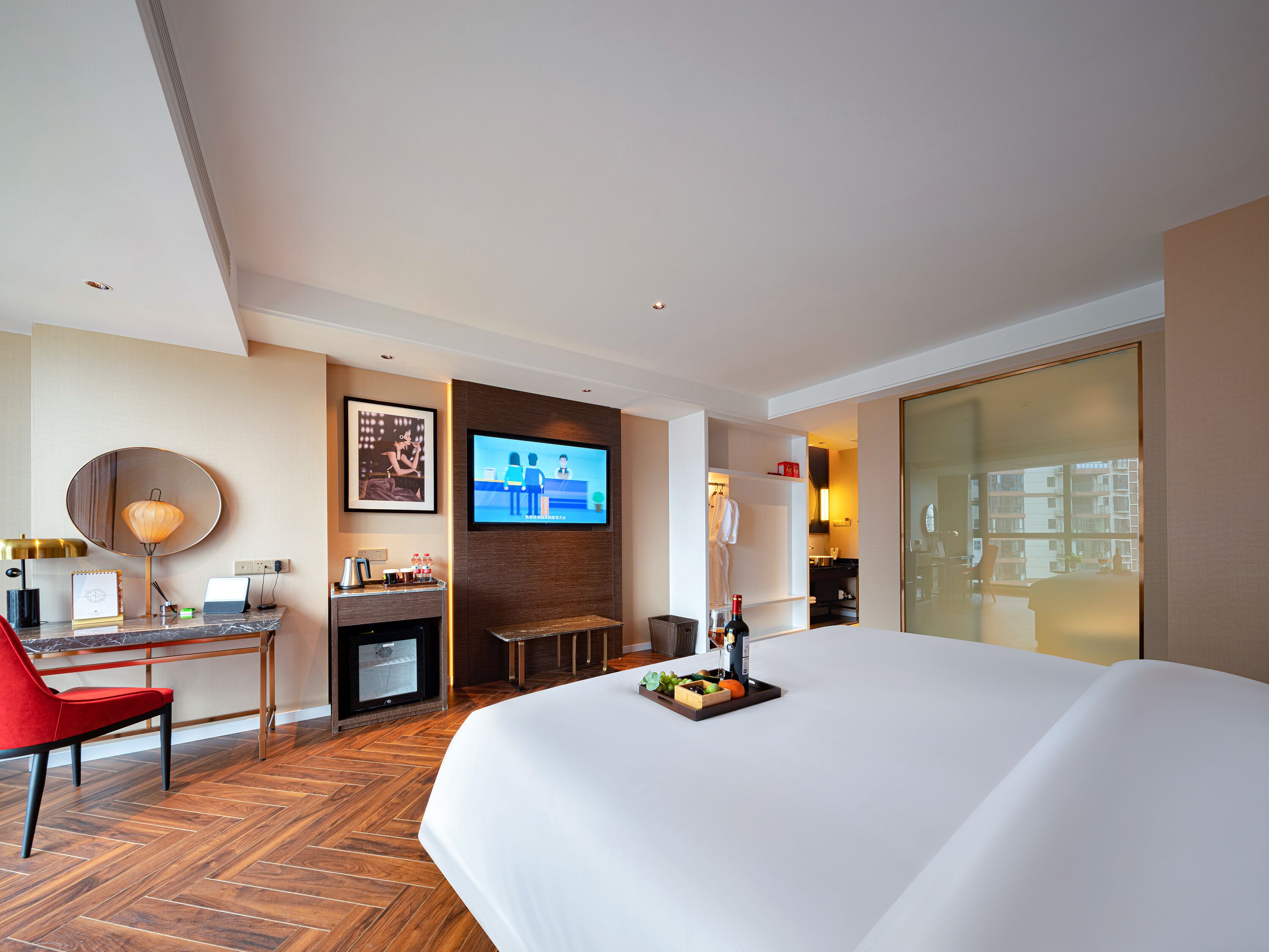 A hotel room with a large bed, a desk with a laptop, a television, and a dining area with fruit.