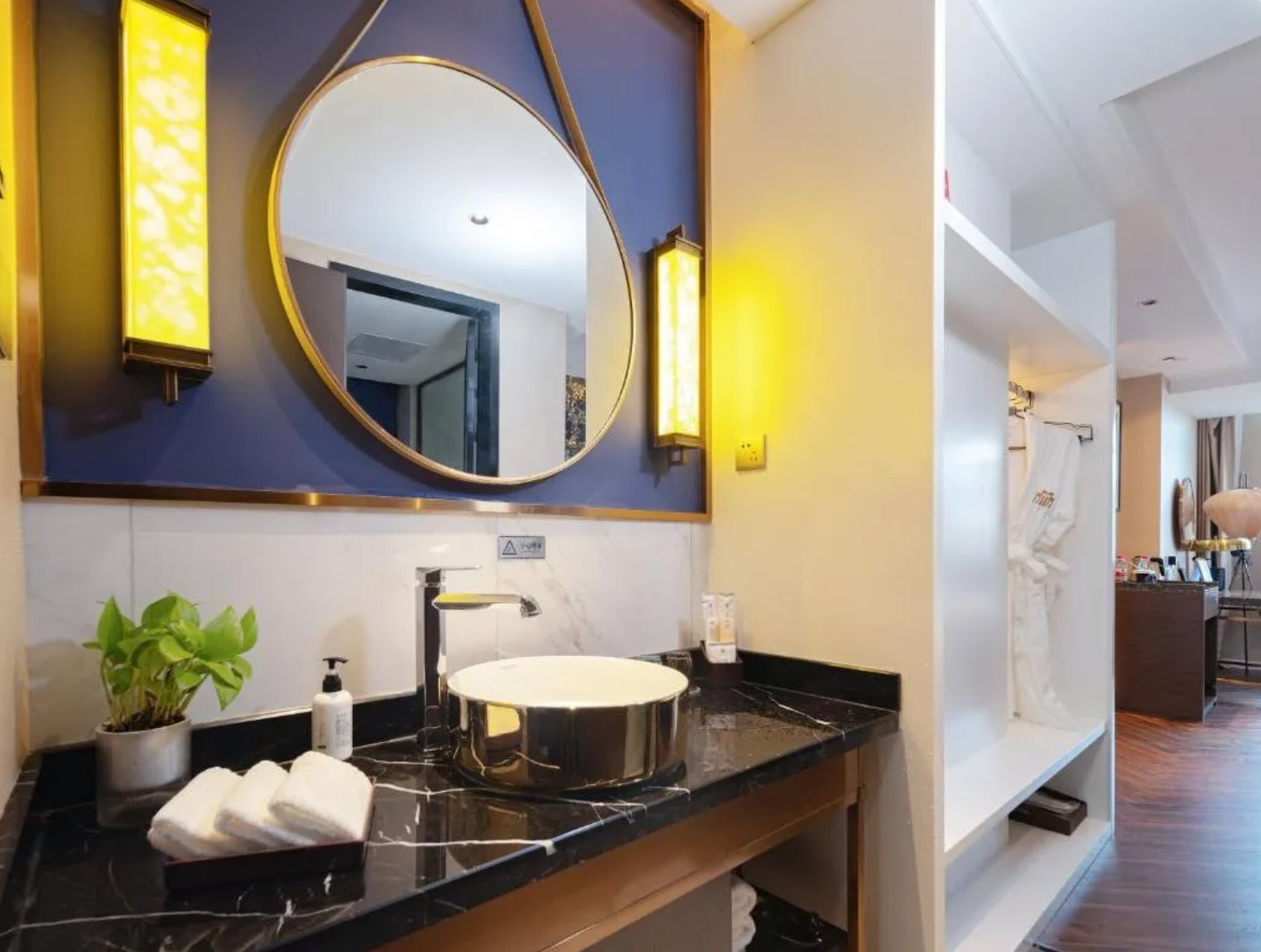 A modern bathroom with a round mirror, a sink, and a potted plant.