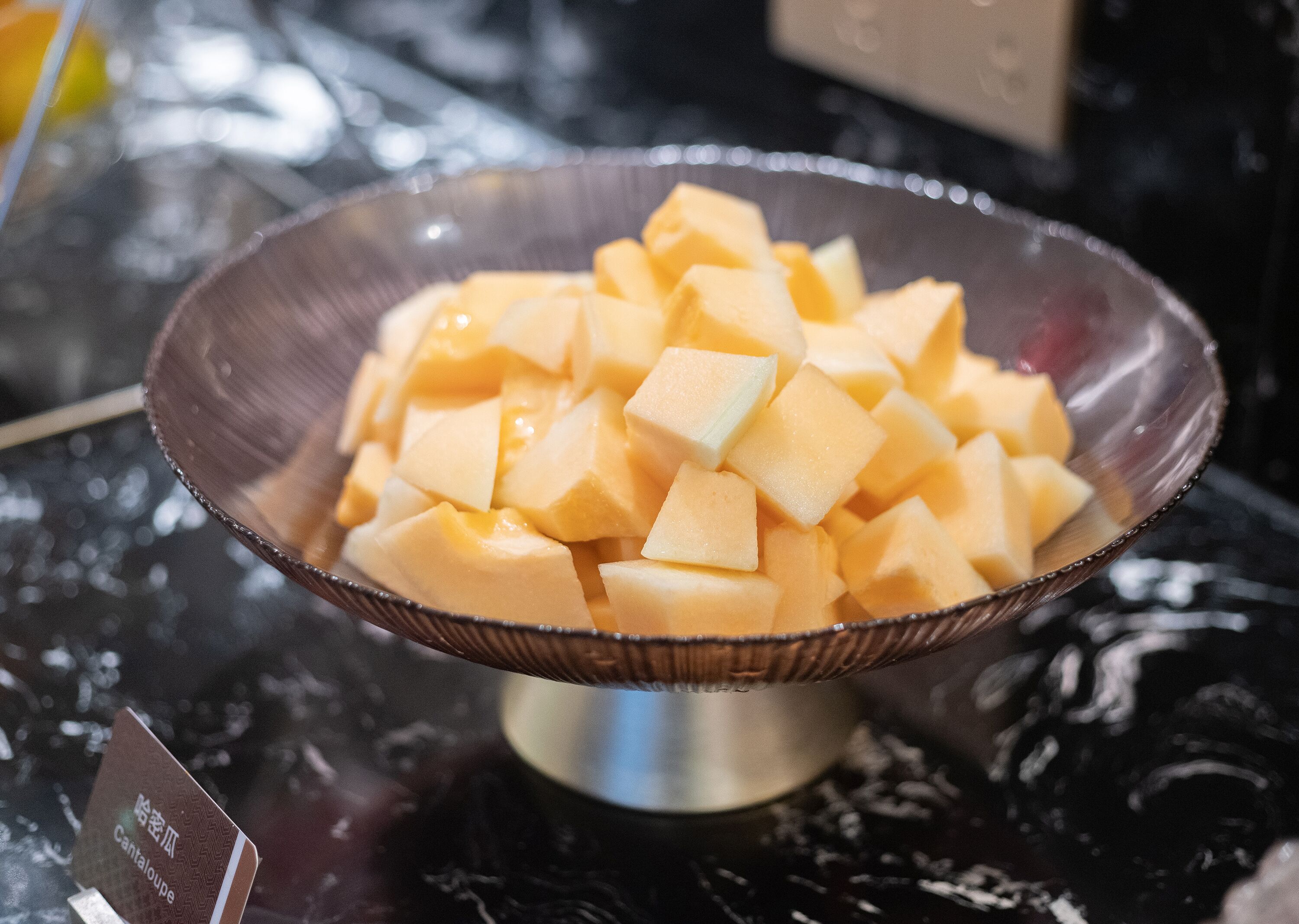 A bowl of cubed cantaloupe on a reflective surface.