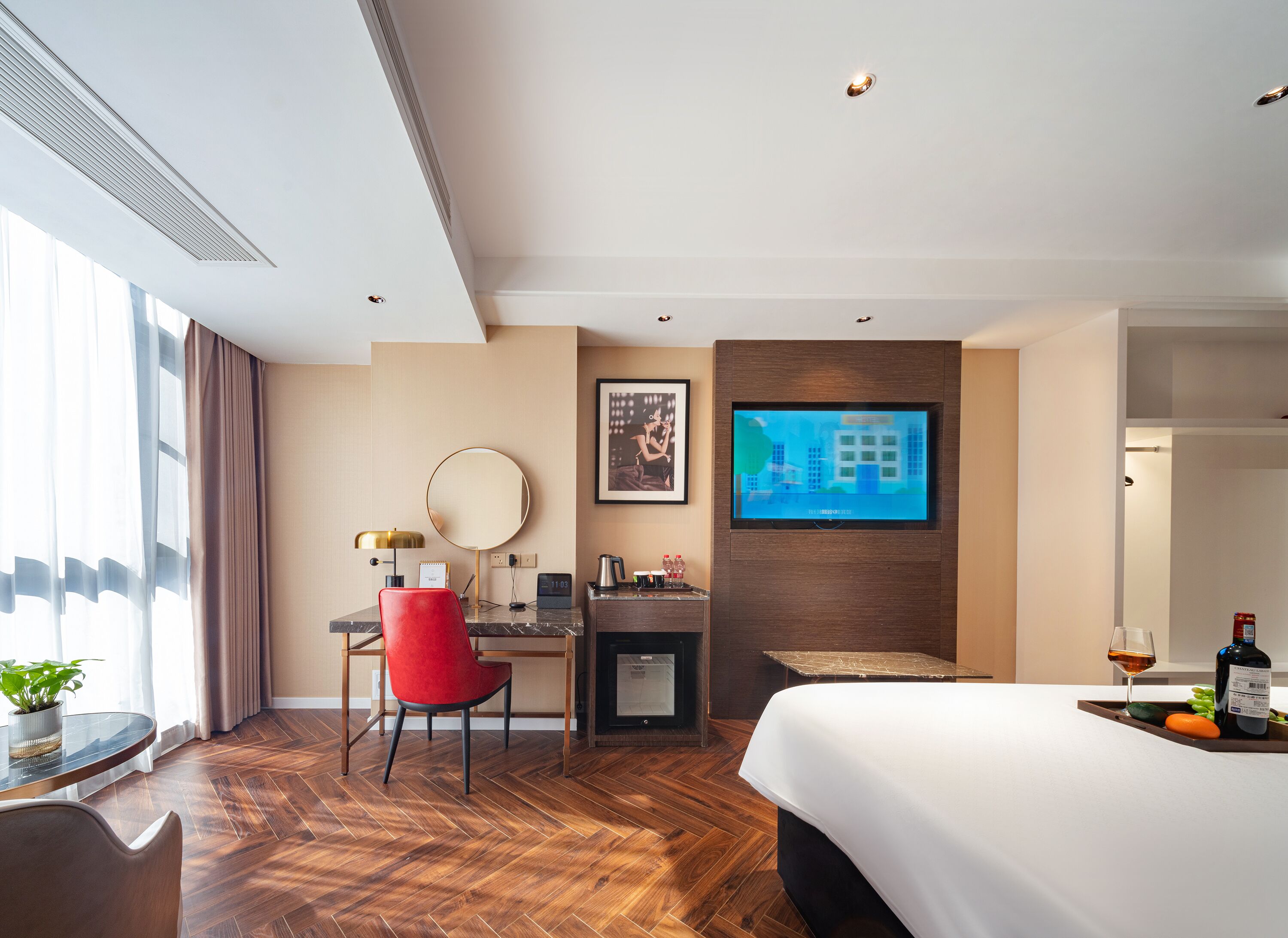 A modern hotel room with a large bed, a desk with a chair, a television, and a small table with a plant.