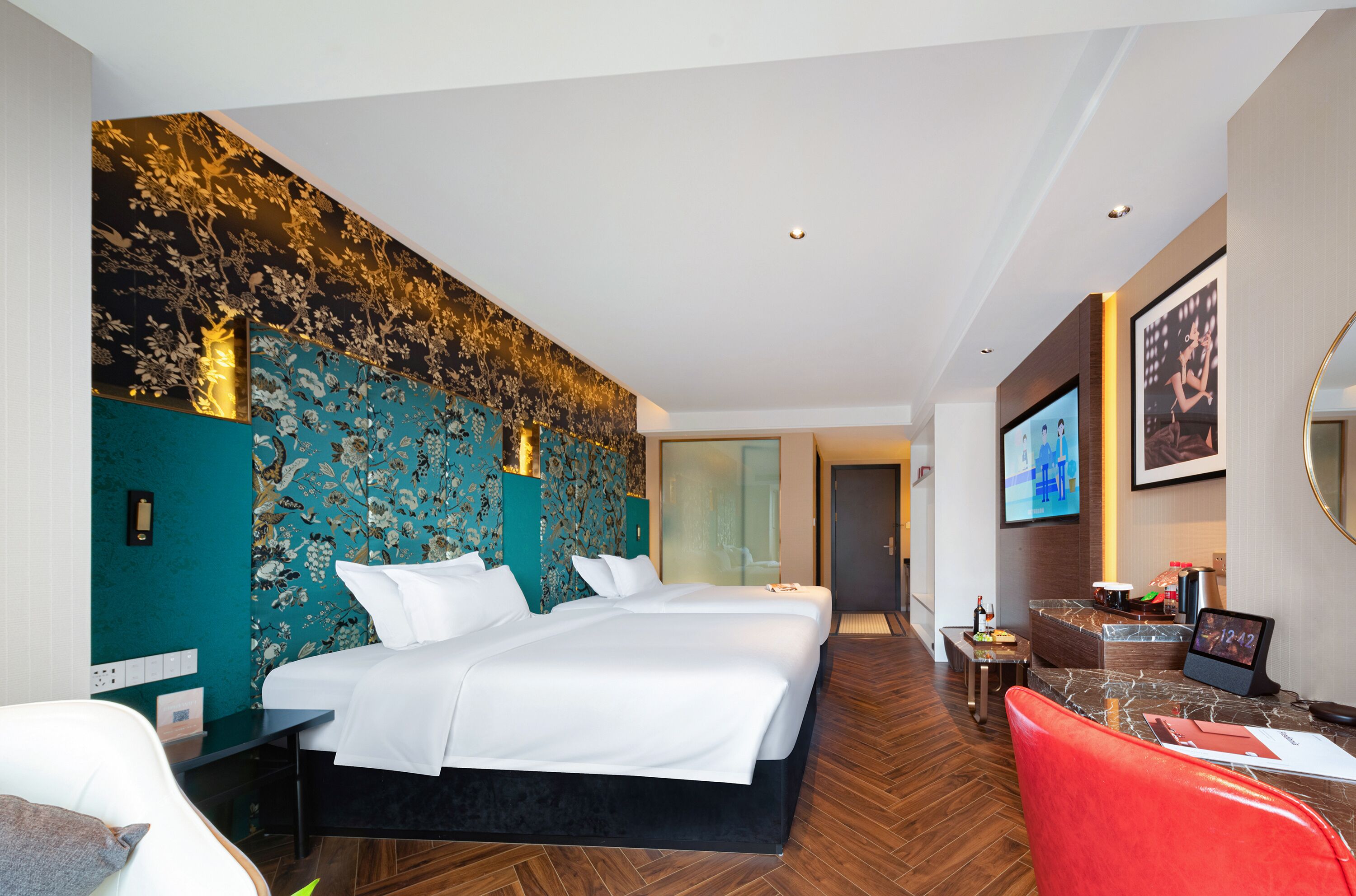 Habitación de hotel moderna con una cama grande, un escritorio con computadora y una zona de estar con una silla roja.
