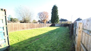 A fenced backyard with grass, a wooden fence, and a tall tree. - Large 3 Bed Bungalow - Beautiful Refurb - Garden (Birmingham)