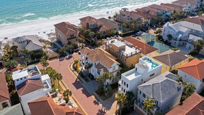 Zona residencial costera con casas de techo rojo, algunas con balcones, y una playa al fondo.