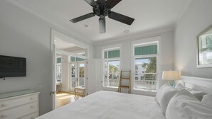 A bedroom with a large bed, a ceiling fan, a TV, and a view of the outside balcony.