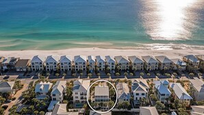 An aerial view of a coastal hotel with a row of beachfront villas, a sandy beach, and the ocean in the background.
