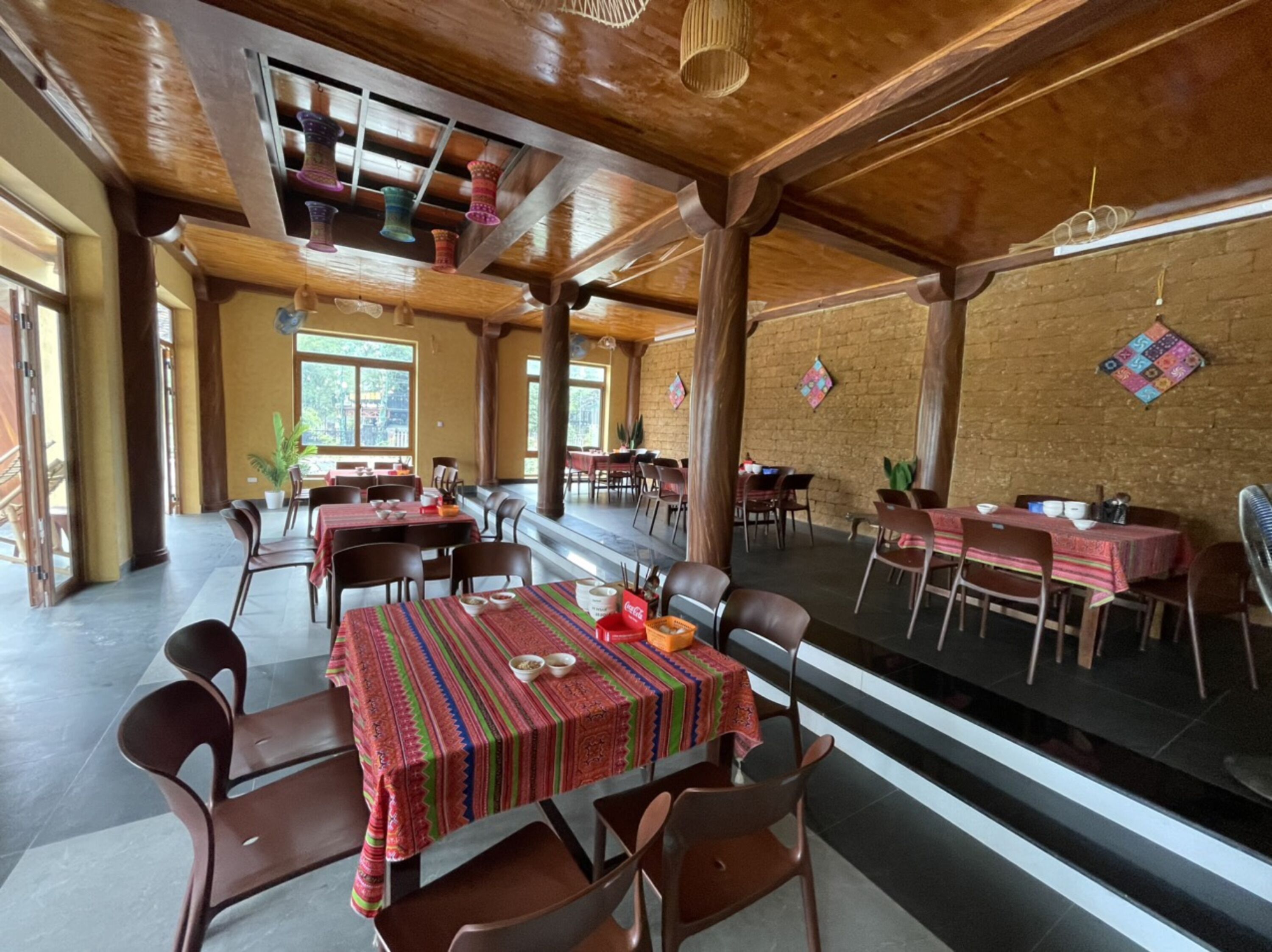Un restaurante con vigas de madera, mesas con manteles de colores y paredes de ladrillo.