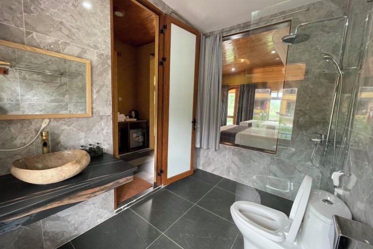 A modern bathroom with a large mirror, a wooden vanity, a glass shower enclosure, and a view of the outdoors.