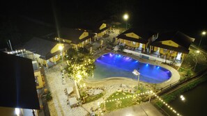 A nighttime view of a hotel with a swimming pool, outdoor seating, and a well-lit garden area. - Sky Bay Lodge (Ha Giang 1)