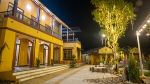 A hotel with a yellow facade, multiple balconies, and outdoor seating areas. - Sky Bay Lodge (Ha Giang 1)