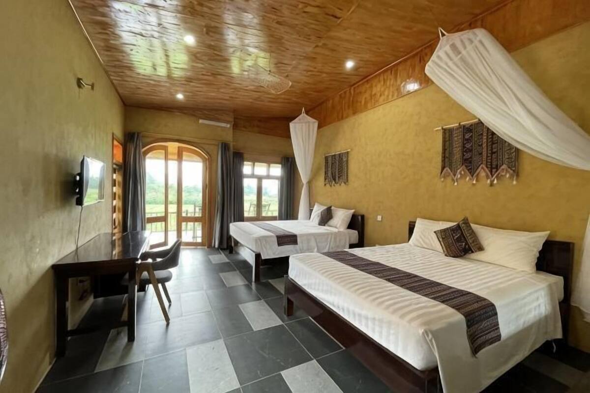 A room with two beds, a desk, a TV, and a large window.