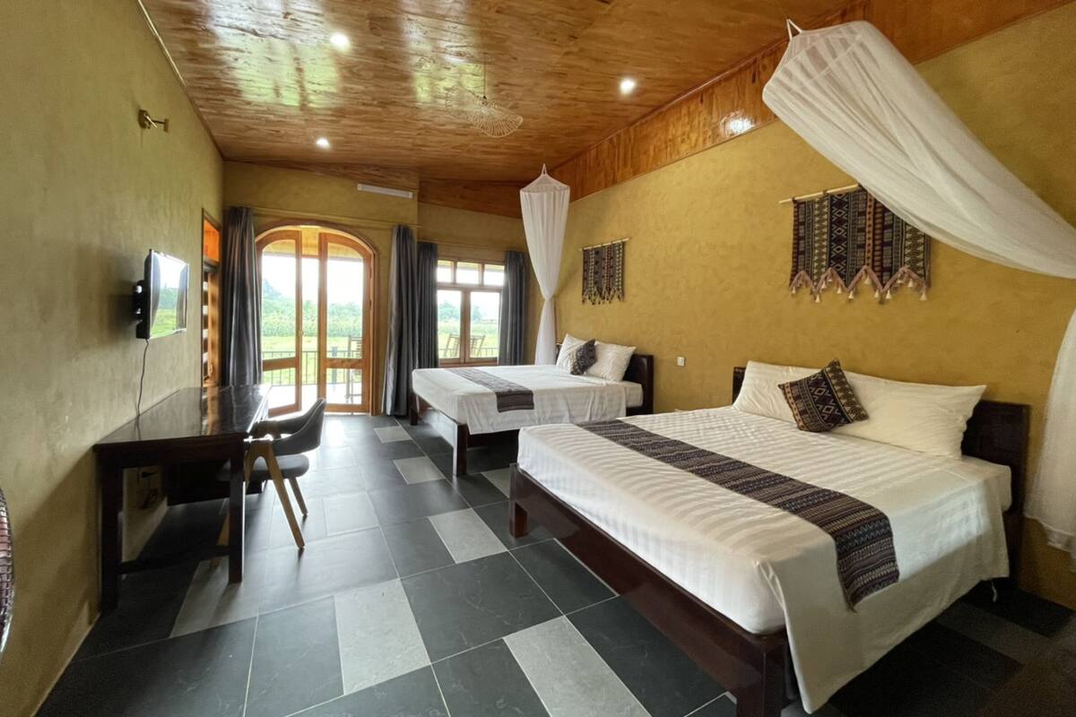 A hotel room with two beds, a desk, and a chair. There is a TV on the wall, and the room has a wooden ceiling and walls.