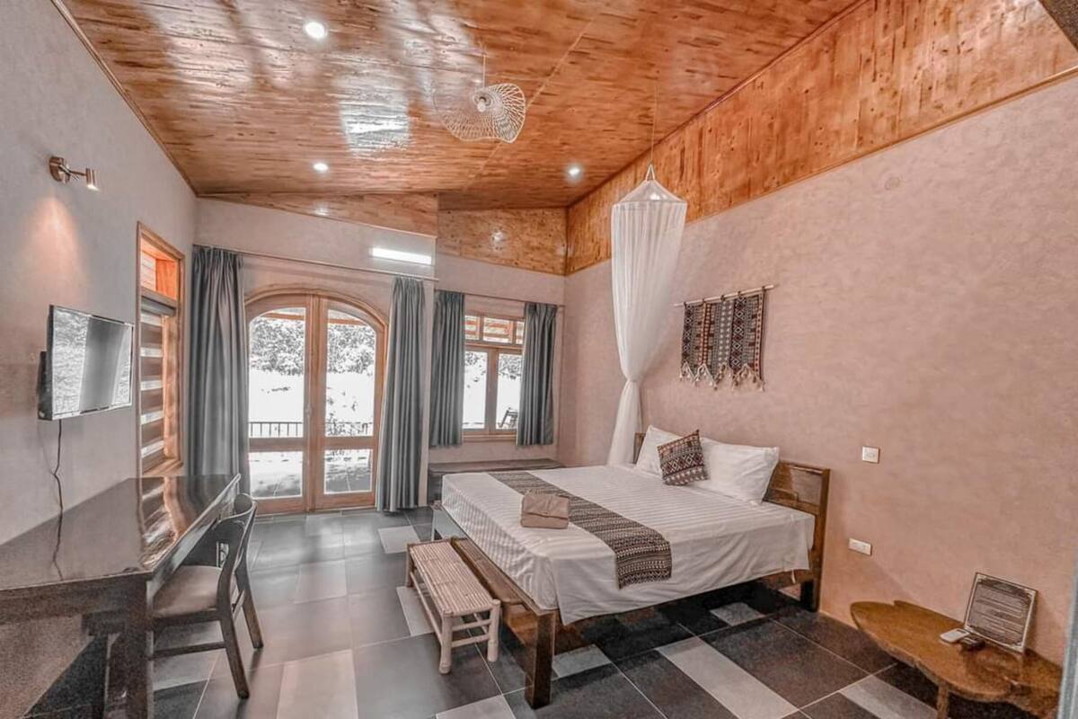 A bedroom with a bed, bench, desk, and a TV.