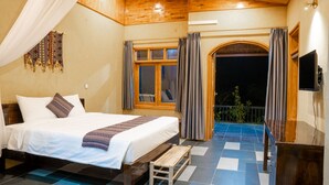 A bedroom with a large bed, a wooden bench, a TV, and a balcony with curtains. - Sky Bay Lodge (Ha Giang 1)