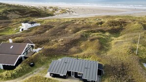 Una propiedad costera con una casa moderna y una edificación más pequeña, rodeada de dunas y una playa.