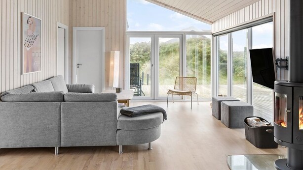 Una sala de estar moderna con un sofá gris, una chimenea y ventanas amplias que ofrecen vistas al exterior.