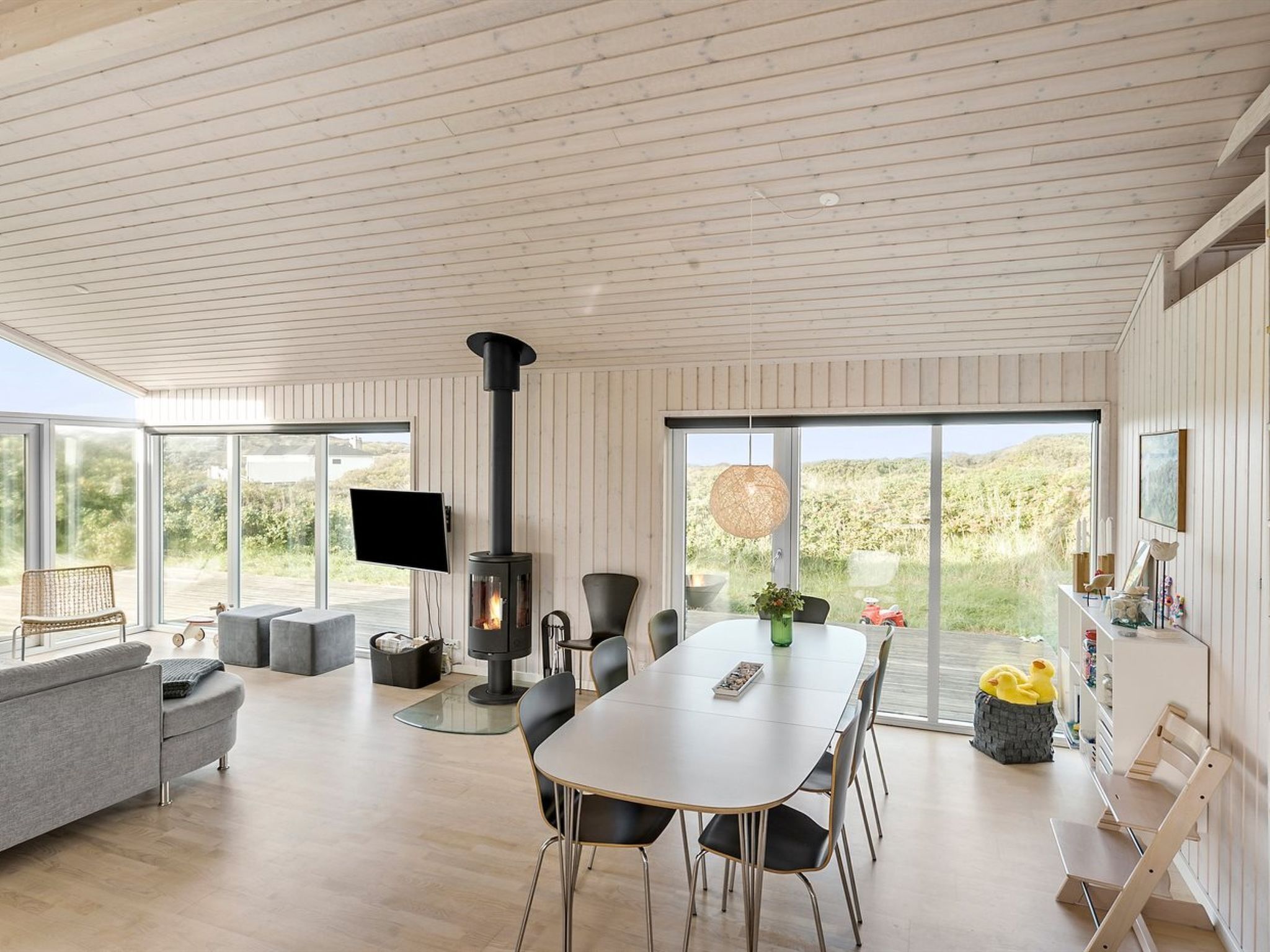 Een moderne woonkamer met een groot raam, een open haard, een eettafel en een bank.