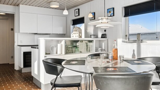 Uma cozinha moderna com armários brancos, uma ilha central e um espaço de refeições com cadeiras de metal e uma mesa redonda.