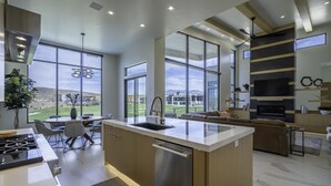 A modern kitchen with a central island, large windows offering a view of the outdoors, and a dining area with a view of the landscape.