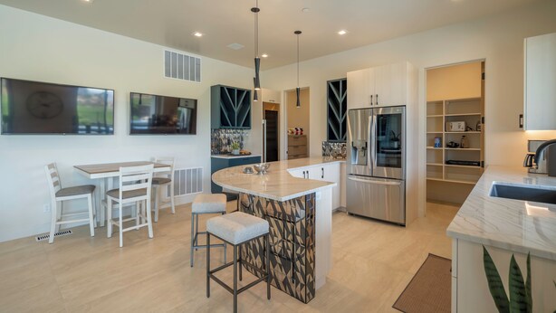 Una cocina moderna con una isla central, electrodomésticos de acero inoxidable y un comedor con mobiliario blanco.