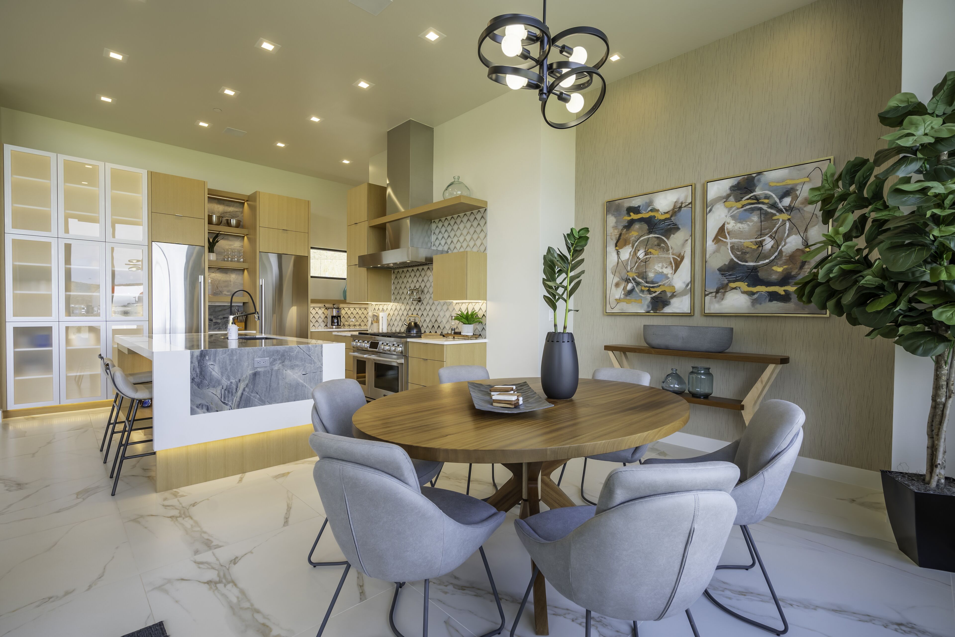 Een moderne keuken met een centraal eiland, inbouwapparatuur en een eethoek met een ronde tafel en stoelen.