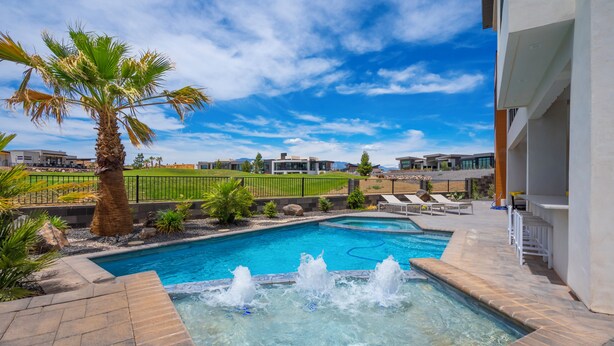 A swimming pool with a hot tub, surrounded by palm trees and a view of modern buildings.