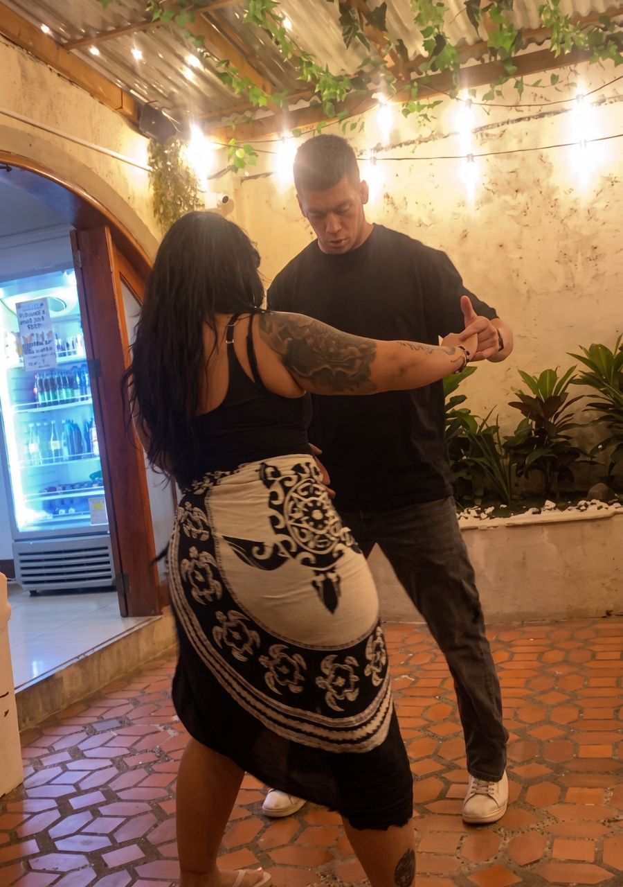 A man and a woman dancing in an outdoor area with a tiled floor, a refrigerator in the background, and plants around.