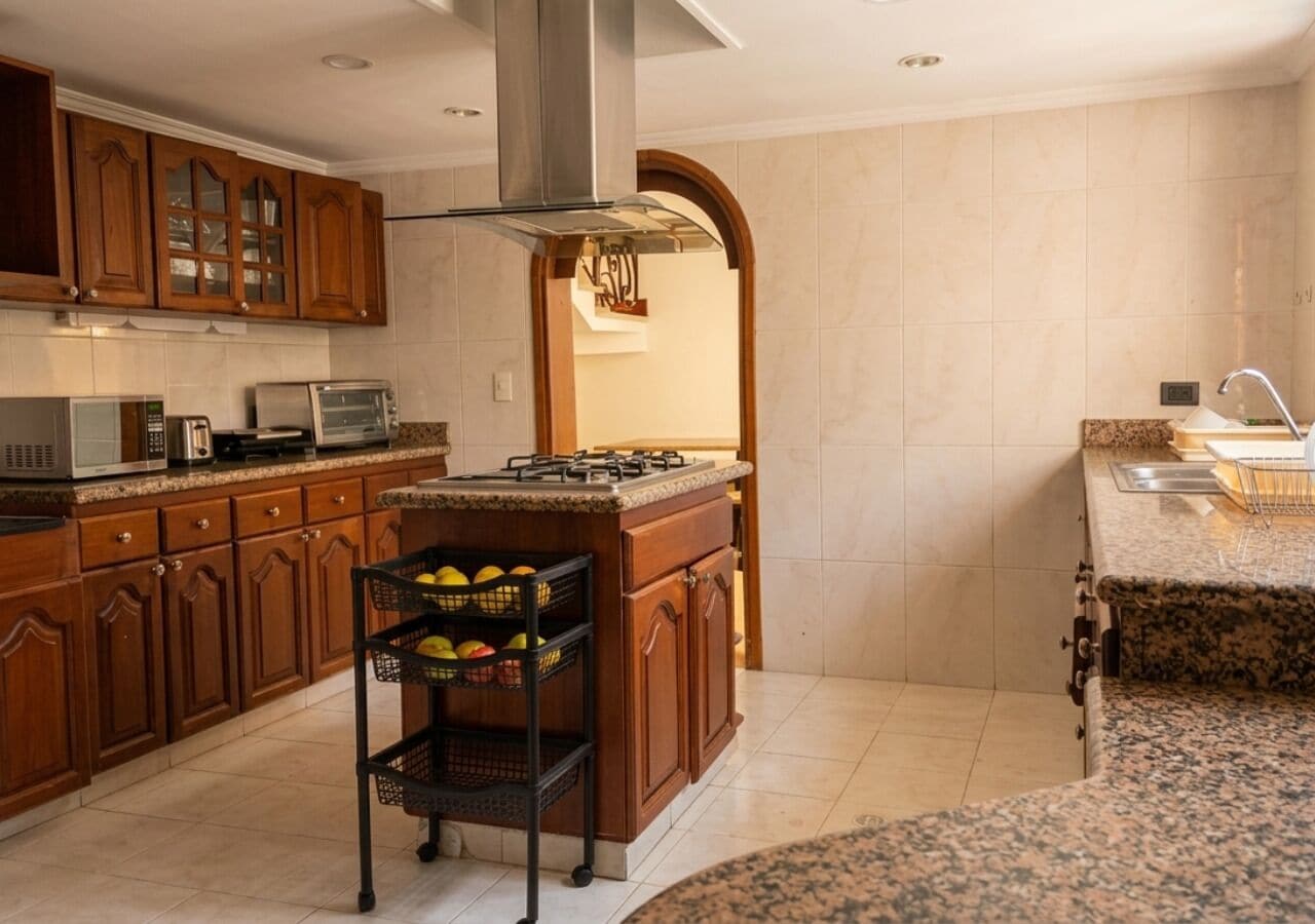 Una cocina con armarios de madera, una campana extractora de acero inoxidable, un microondas empotrado, un tostador y una cesta de frutas.