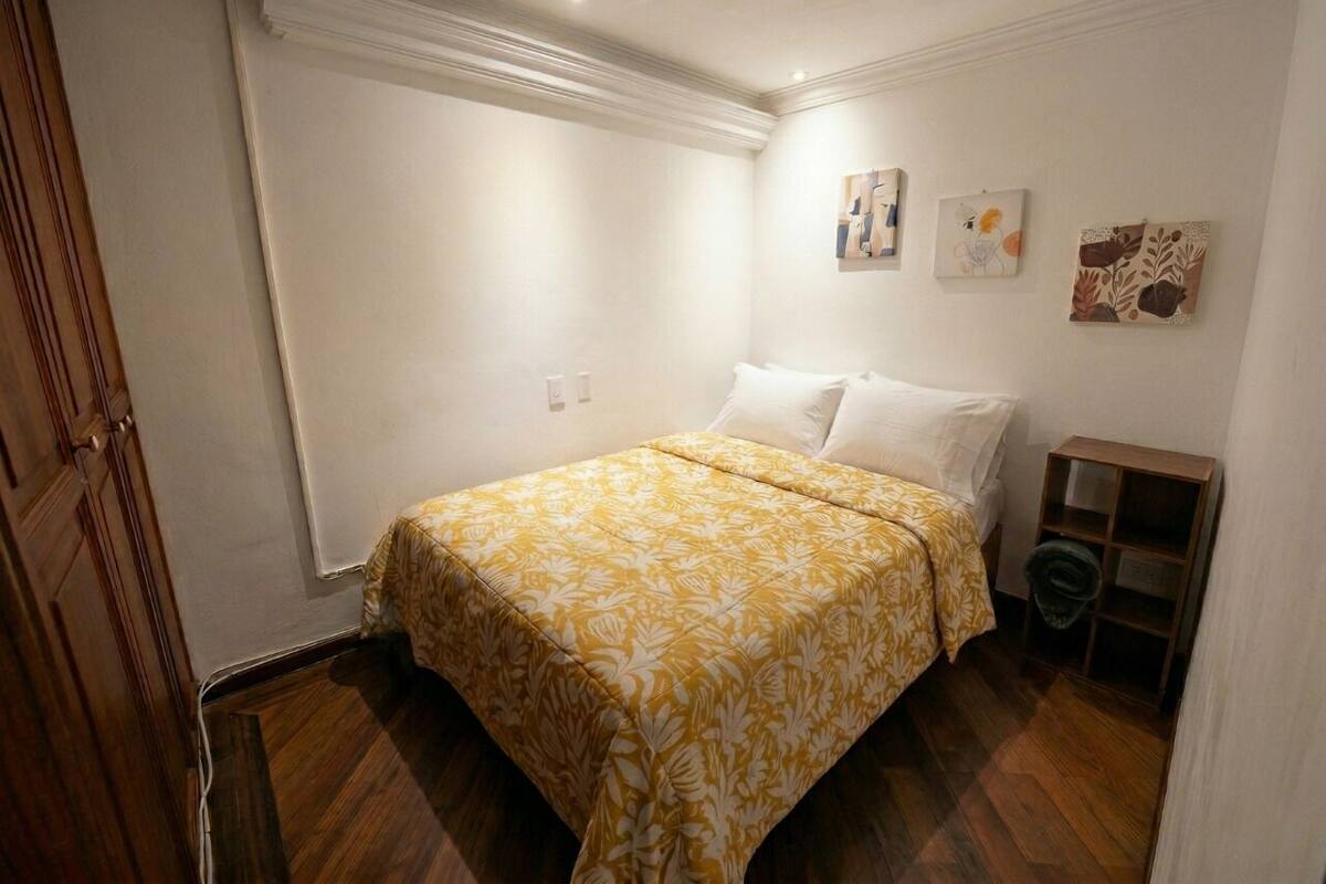 Un dormitorio con cama, paredes blancas y suelo de madera.