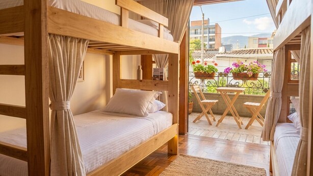A room with a bunk bed, a small table with chairs, and a balcony with potted plants.