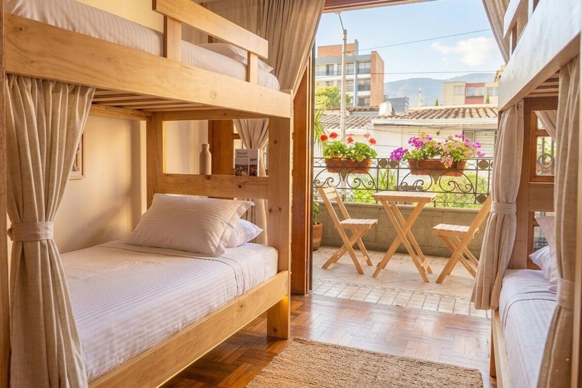 Una habitación con literas, una mesita con sillas y un balcón con plantas en macetas.
