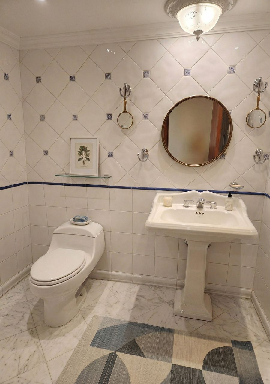 A bathroom with a toilet, sink, mirror, and decorative tiles.