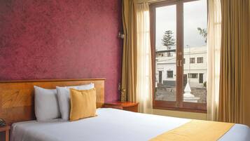 A hotel room with a bed, a wooden headboard, a nightstand, and a window with curtains.