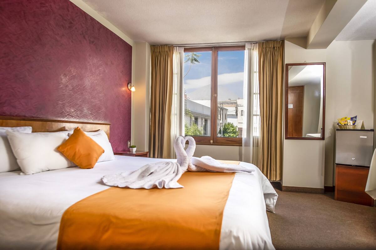 A hotel room with a bed, a nightstand, a mirror, and a window with curtains.