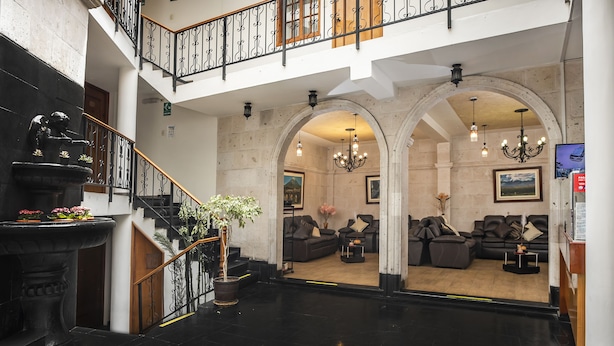 A lobby with a staircase, black tiled floor, a fountain, and a seating area with sofas and a TV. - Maison du Soleil (Arequipa)