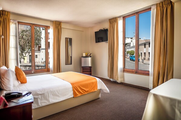 Une chambre d’hôtel avec un lit, une télévision, une petite table et une fenêtre avec des rideaux.
